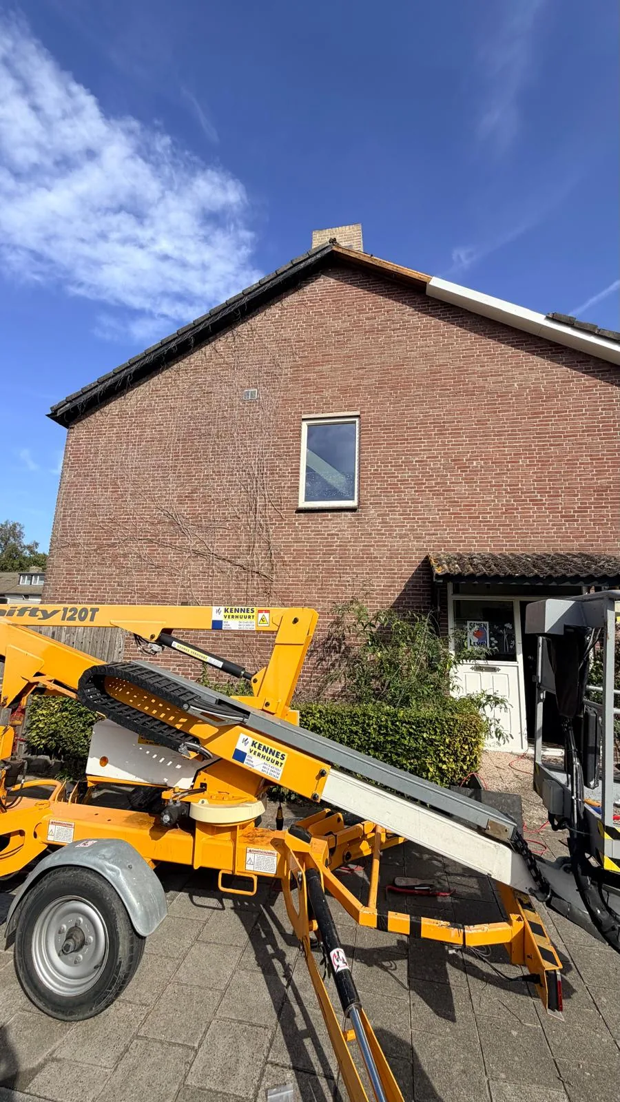 De hoogwerker voor de kopgevel van de woning in Boxtel tijdens het vervangen van de overstek, met resten klimop nog op de gevel